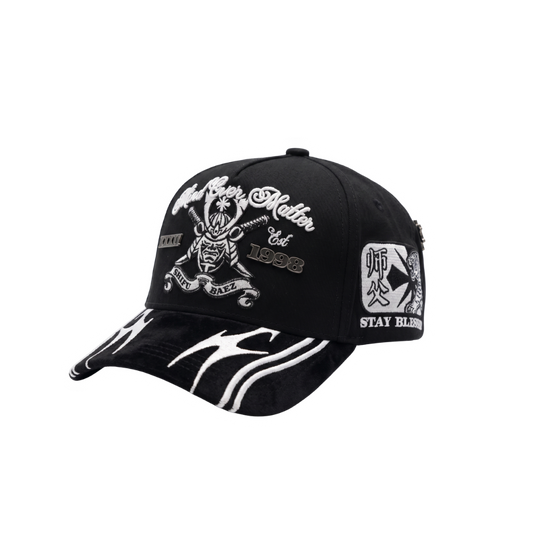 Gorra Mind Over Matter negra con bordado frontal blanco de figura central, tipografía decorativa y visera con gráficos blancos en contraste