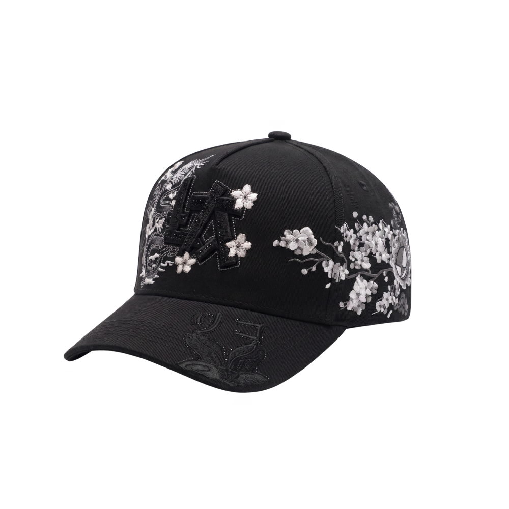 Gorra LA Japan negra con aplique frontal LA negro, dragon y flores blancas al frente, graficos laterales oscuros con detalles rojos y visera curva negra.
