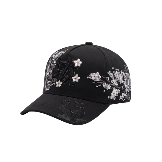 Gorra LA Japan negra con aplique frontal LA negro, dragon y flores blancas al frente, graficos laterales oscuros con detalles rojos y visera curva negra.